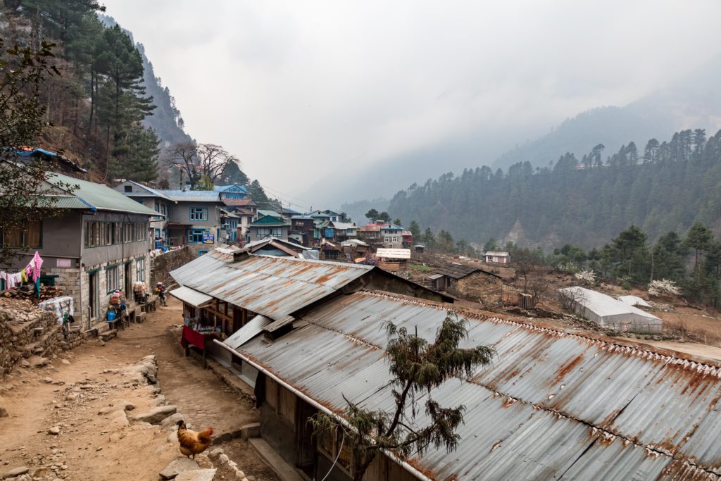 A high altitude village in the Himalayas with a rustic tin roof, chicken wandering free and aspects of a rustic life in the mountains.
