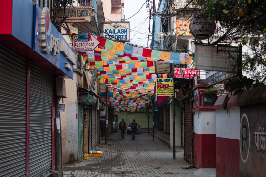 Prayer flags line a street in Kathmandu Nepal. Bright colors contrasting the alleyway
