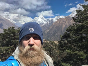 Self-portrait of a trekker with a snowy Himalayan range behind, taken above Namche Bazaar on the Everest Base Camp trail