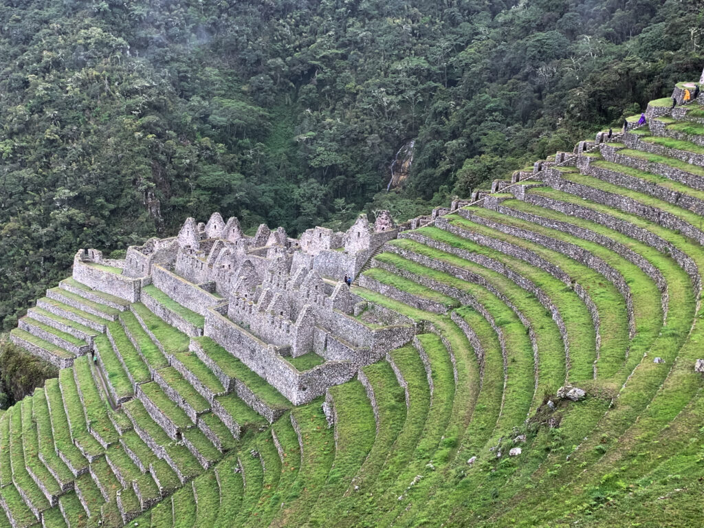 Aerial view of the Wiñay Wayna Incan ruins with curved agricultural terraces set against a lush, green jungle backdrop on the Inca Trail.