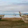Color analog multiple exposure photograph of abandoned wooden fishing boats along Puerto Natales Harbor in Patagonia, Chile, with mountains and a vessel in the distance.